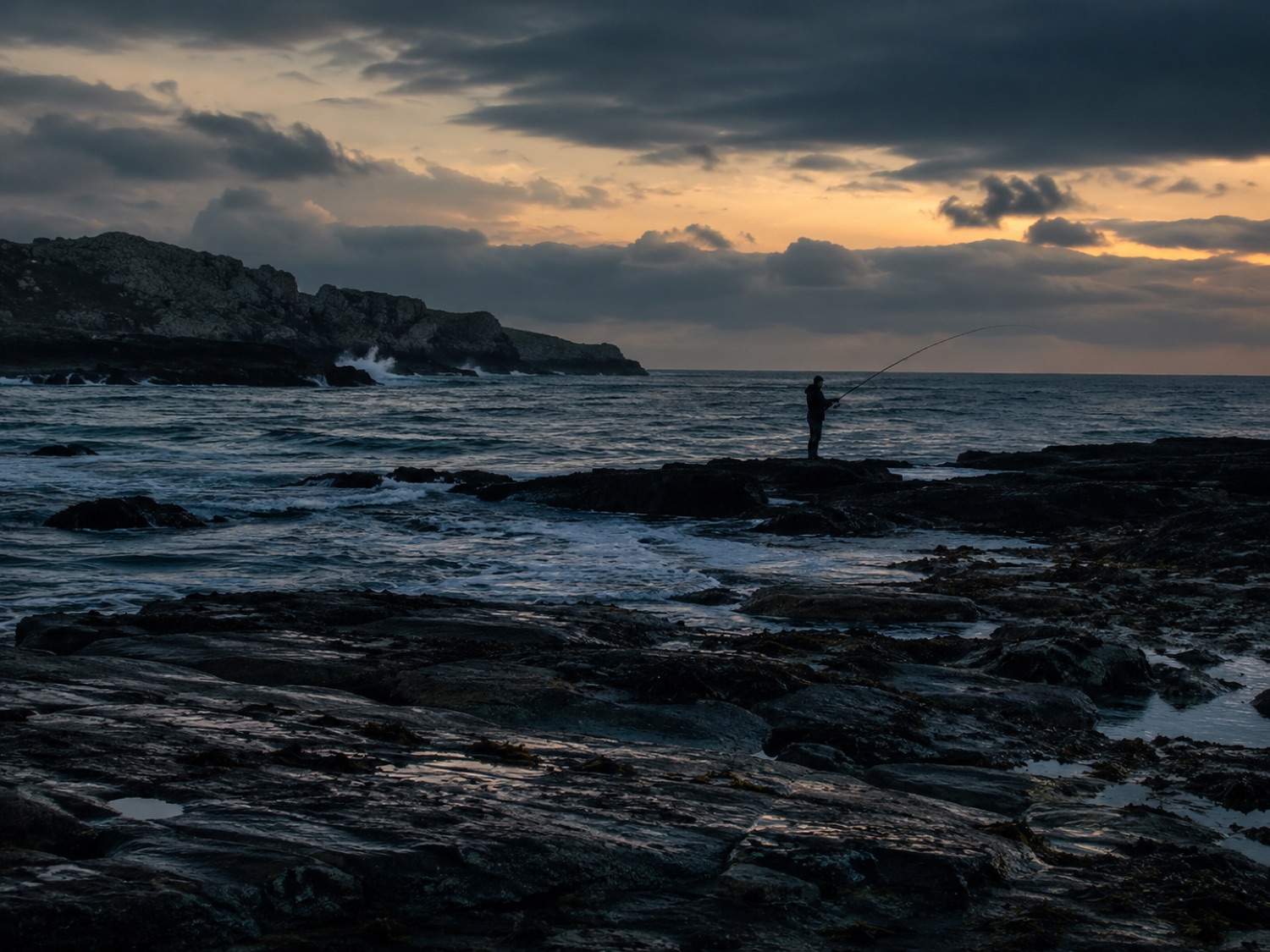 Un pêcheur en bord de mer au coucher du soleil